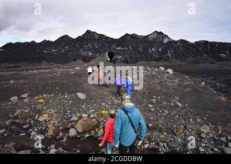 Eine Reisegruppe geht in Richtung der Katla Eishöhle im Kotlujokull Gletscher, einem Auslaufgletscher von Myrdalsjokull. Der Gletscher ist mit vulkanischer Asche bedeckt. Stockfoto