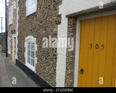 Reihenhaus Nummer 305 mit einer senfgelben Eingangstür & Kiesel, die an den Außenwänden platzen; typische Strandverkleidung für Suffolk-Häuser Stockfoto