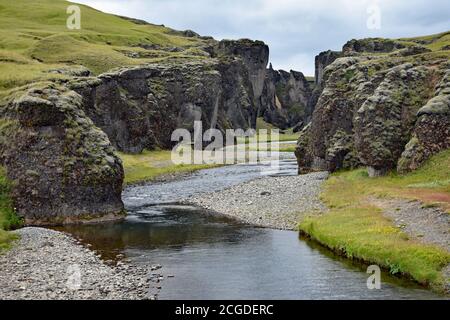 Der Eingang zum Fjadrargljufur Canyon. Die Flüsse Fjaðrá, die durch die Serpentinenschlucht fließen. Grünes Moos bedeckt die Felswand. Südisland. Stockfoto