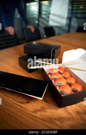 Sushi-Rollen-Lieferkarton am Arbeitsplatz mit Essstäbchen. Mittagessen im Büro Stockfoto