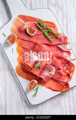 Köstlicher Serrano-Schinken mit frischen Feigen und Rosmarin auf Weiß Schneidebrett Stockfoto