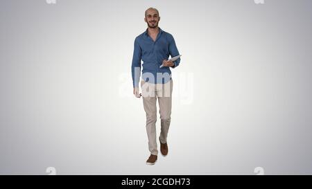 Arab Presenter zu Fuß mit digitalen Tablet Wischen Seiten auf sie auf Gradienten Hintergrund. Stockfoto