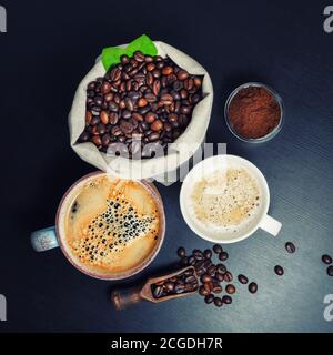 Stillleben mit Kaffeetassen und Kaffeebohnen in Leinenbeutel auf schwarzem Küchentisch. Draufsicht. Flach liegend. Stockfoto