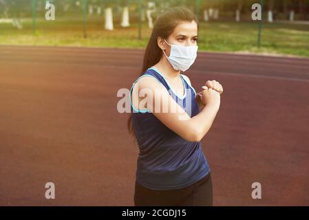 Ein junges Mädchen geht in einer Schutzmaske auf die Straße zum Sport. Sport in Quarantäne, Coronavirus, covid-19 Konzept. Stockfoto