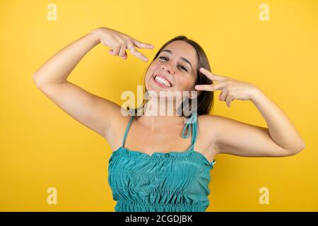 Junge schöne Frau über isolierten gelben Hintergrund tun Frieden Symbol mit Fingern über Gesicht, lächelnd fröhlich zeigt Sieg Stockfoto