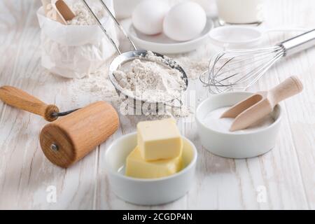 Dinkelmehl, Zucker mit Backzutaten und Küchenutensilien auf weißem Holztisch. Stockfoto