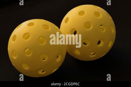 Zwei Picklebulle auf einem schwarzen. Pickleball hat sich zum am schnellsten wachsenden Sport in Amerika, auf einem Platz gespielt 1/4 Größe eines Tennisplatzes. Stockfoto