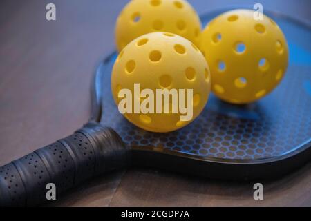 Pickleballs und ein Paddel. Pickleball hat sich zum am schnellsten wachsenden Sport in Amerika, auf einem Platz gespielt 1/4 Größe eines Tennisplatzes. Stockfoto