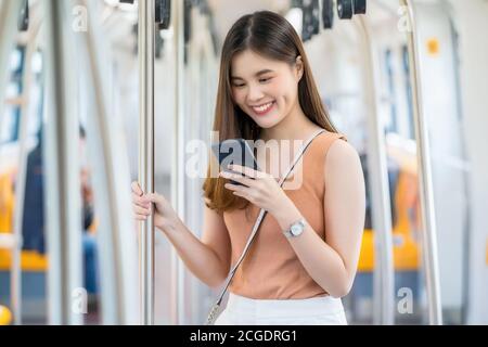 Junge asiatische Frau Passagier mit Smartphone und Blick auf außerhalb der U-Bahn-Zug, wenn Sie in der Großstadt, Pendler und Transport Co Stockfoto