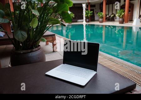 Weißer Laptop auf dem Hintergrund des Schwimmbades. Konzeptioneller Arbeitsbereich. Freiberufler, Reise- und Urlaubskonzepte. Stockfoto