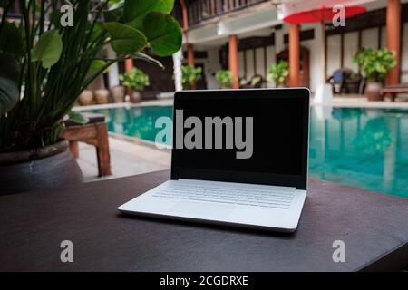 Weißer Laptop auf dem Hintergrund des Schwimmbades. Konzeptioneller Arbeitsbereich. Freiberufler, Reise- und Urlaubskonzepte. Stockfoto