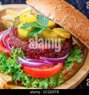 Pflanzenbasierter veganer Rübenburger mit Gurken frischer Salat, Tomaten, rote Zwiebeln im Brötchen mit Sesamsamen darauf, französische Braten, Ketchup auf Bambus Stockfoto