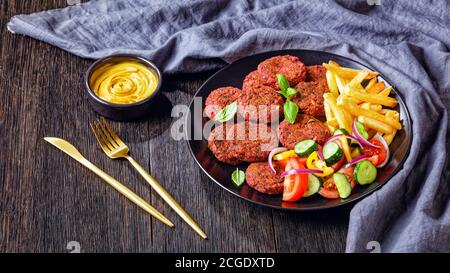 Vegane Rote Bete, Pilze, schwarze Bohnenpasteten mit pommes Frites und Tomaten serviert, Gurken roten Zwiebelsalat auf einem schwarzen Teller mit Nährhefe sa Stockfoto