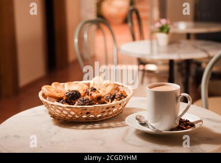 tasse Kaffee, auf Marmortisch, mit Gebäck in Korbkorb, Cafeteria Tische Hintergrund Stockfoto