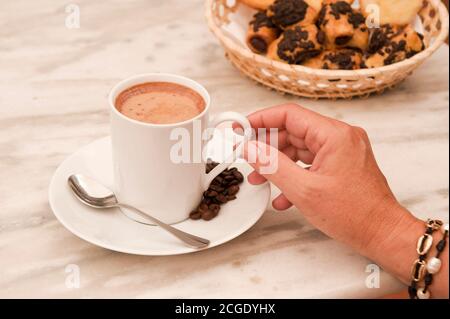 tasse Kaffee mit Frauenhand, auf Marmortisch, mit Gebäck im Korbkorb Stockfoto