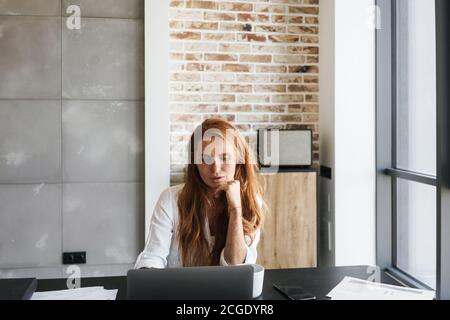 Bild von serious Rotschopf Geschäftsfrau arbeiten mit Laptop während des Sitzens Am Tisch zu Hause Stockfoto