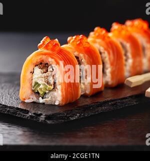 Japanische Küche. Lachs-Sushi Rollen in Essstäbchen auf einem Steinteller über betoniertem Hintergrund. Stockfoto