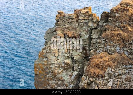 Ein Felsen an der Küste, zerbröckelt durch Erosion, Wind und Klima, mit Rissen und zerbröckelnden Steinen bedeckt mit Moos und Flechten. Stockfoto