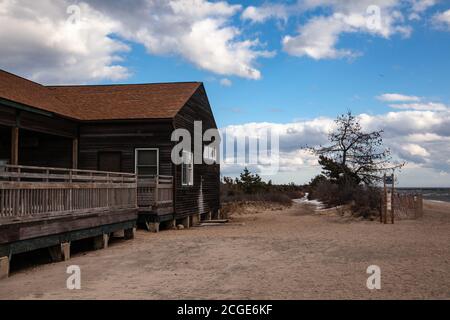 Einstöckiges Haus aus dunklem Holz mit einer Terrasse Am Sandstrand in der Nähe des Wassers und hell Blauer Himmel mit großen weißen Wolken auf dem Hintergrund Stockfoto