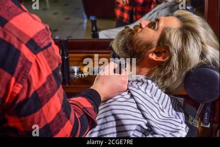 Bärtig und stilvoll. Hipster Mann mit Bart schneiden seine Haare in einem Friseurladen. Professionelle Friseurarbeit. Lifestyle. Master Barber macht die Frisur und Styling mit Trockner. Konzept Barbershop. Stockfoto