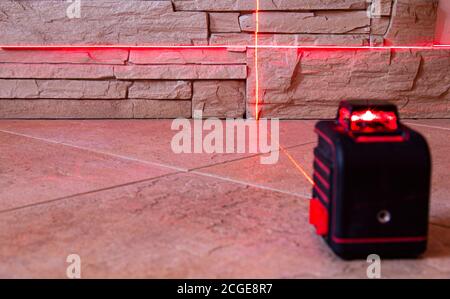 Die roten Lichtstrahlen des Laserpegelgeräts an Wand und Boden zeigen die Richtung an. Copyspace für Text. Stockfoto