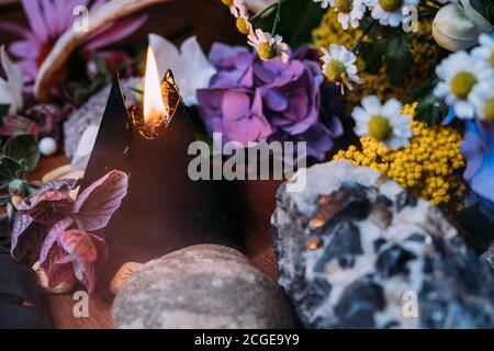 Stillleben mit brennender schwarzer Kerze, Steinen und Kräutern Hintergrund. Schwarzes magisches Ritual mit okkulten, bösen und esoterischen Symbolen. Halloween oder Weissagung Stockfoto