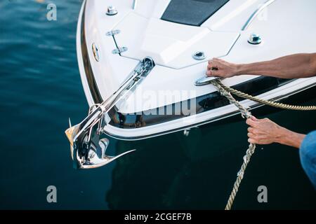 Mann s Hand mit Bootsseil. Der Segler moort sein Motorboot an der Anlegestelle. Nahaufnahme Hände und Bogen des Bootes. Stockfoto