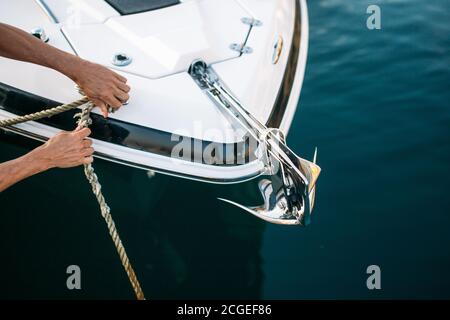 Mann s Hand mit Bootsseil. Der Segler moort sein Motorboot an der Anlegestelle. Nahaufnahme Hände und Bogen des Bootes. Stockfoto