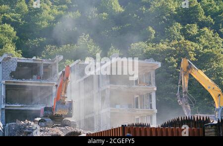 Großer gelber Bagger bricht im Sommer altes Haus ab Stockfoto