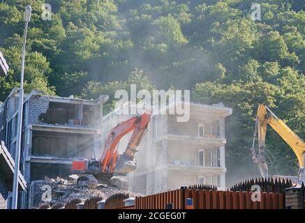 Großer gelber Bagger bricht im Sommer altes Haus ab Stockfoto