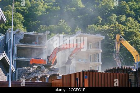 Großer gelber Bagger bricht im Sommer altes Haus ab Stockfoto