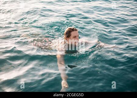 Junger Mann schwimmt am Meerwasser, genießt Freiwasserraum und warmes ruhiges Wasser. Stockfoto