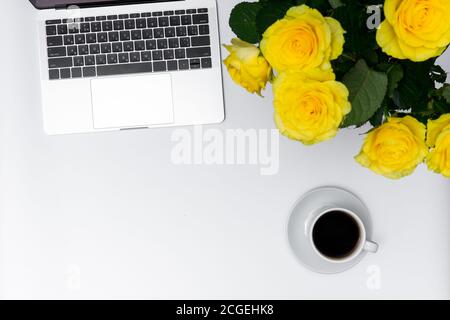 Weiblicher Arbeitsplatz, gelbe Rosen, Laptop und Becher auf weißem Hintergrund Stockfoto