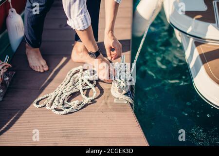 Männliche Hände mit Bootsseil. Segler binden Seeknoten während der Anlegestelle der Yacht. Nahaufnahme der Hände Stockfoto