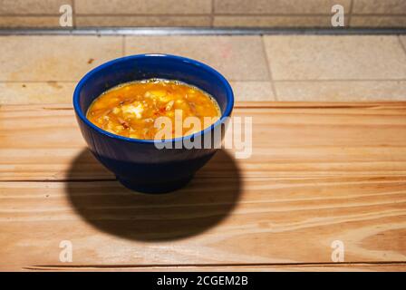 Locro, typische und traditionelle argentinische Küche, serviert in einem blauen Behälter auf einem Holzbrett, begleitet von Brot und einem Glas Wein, mit Löffeln. Sel Stockfoto