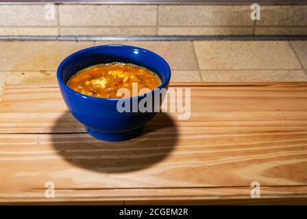 Locro, typische und traditionelle argentinische Küche, serviert in einem blauen Behälter auf einem Holzbrett, begleitet von Brot und einem Glas Wein, mit Löffeln. Sel Stockfoto