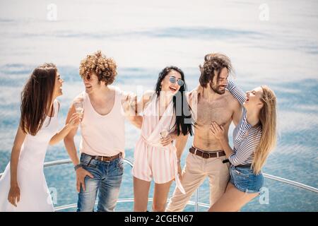 Zwei reichen Kerle in Yacht Party mit schönen Damen auf Segelboot. Außenaufnahme der jungen Menschen über das Meer und den blauen Horizont posiert mit Copyspace Stockfoto