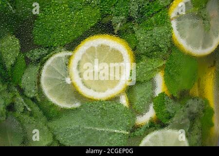 Hintergrund von Zitronen und Minze in einem kalten Glasbehälter. Frische Zitronen und Minzlimonade in einer Flasche Nahaufnahme. Glas mit Wassertröpfchen bedeckt. Natur Stockfoto