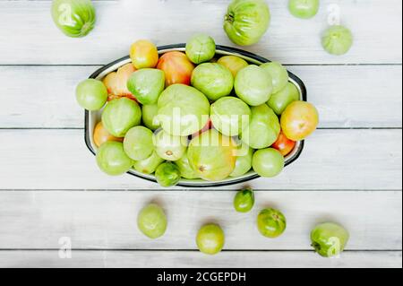 Viele grüne unreife Tomaten in Metall Tasse auf hellem Holzhintergrund, Draufsicht, selektiver Fokus Stockfoto