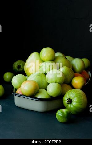 Viele grüne unreife Tomaten in Wassertropfen in einem Metal Cup auf dunklem Hintergrund Stockfoto