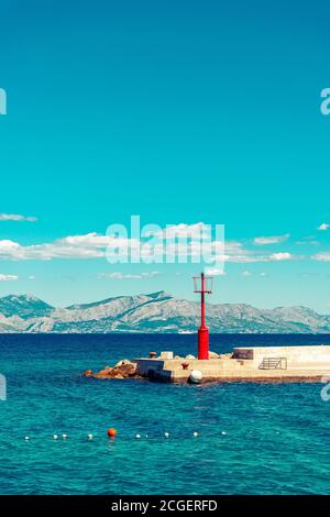 Schöne Seeslandschaft, Pier mit Leuchtturm gegen felsige Küste und klaren blauen Himmel. Stockfoto