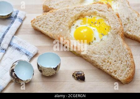 Gebratenes Stück Brot mit Wachtelei auf einem hölzernen Schneidebrett mit einem Küchentuch und Eierschalen, selektiver Fokus. Gesunde Ernährung Konzept. Stockfoto