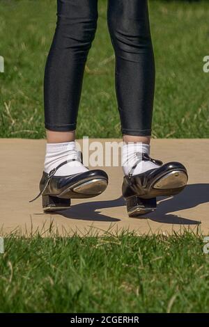 Beine und Füße eines jungen Mädchens in schwarzen Steppschuhen, weißen Socken und schwarzen Strumpfhosen. Tanzen Stepptanz im Freien . Low-Angle-Aufnahme. Ansicht schließen. Stockfoto