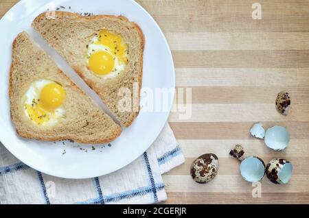 Sandwiches mit gebratenen Wachteleiern auf einem weißen Teller auf einem hölzernen Schneidebrett mit einem Küchentuch und Eierschalen, Draufsicht mit Kopierplatz. Stockfoto