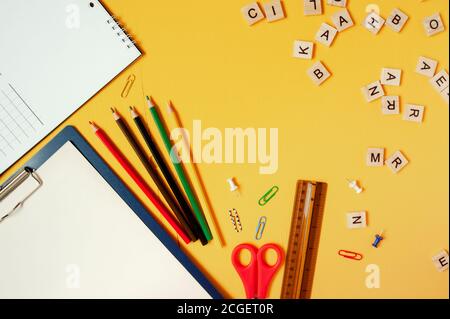 Schullayout, Schulbedarf und Zubehör auf hellgelbem Hintergrund und verstreuten Holzbuchstaben Stockfoto