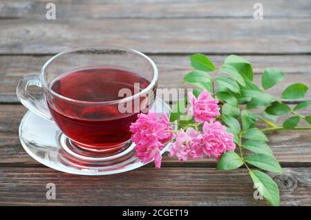 Tasse frisch zubereiteter heißer Tee und rosa Rosen auf einem alten Holztisch. Stockfoto