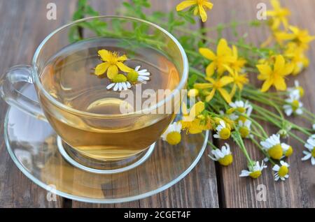 Frisch zubereiteter Johanniskraut-Tee mit Kamille in einer Glasschale und frischen Blumen auf einem Holztisch aus der Nähe. Gesundes Teekonzept Stockfoto