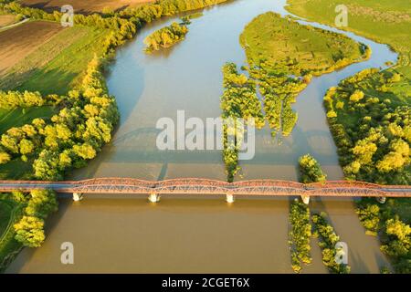 Luftaufnahme einer schmalen Straßenbrücke, die sich über einen schlammigen, breiten Fluss in grüner ländlicher Umgebung erstreckt. Stockfoto