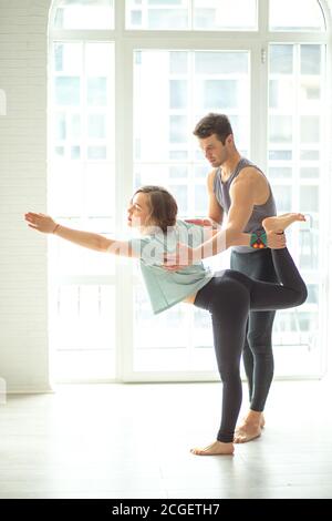 Professionelle Yoga männlichen Lehrer hilft weiblichen Anfänger Asana gegen große Fenster in hellen sonnigen Studio zu machen. Der Meister hilft seinem Schüler, yog zu machen Stockfoto