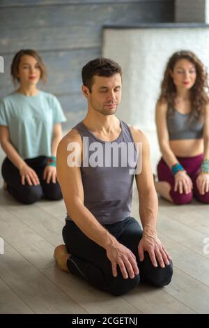 Hübscher junger muskulöser Mann, Yogi-Lehrer, der kaukasischen Frauen Yoga leitet. Gruppenschulung. Gesundes Lifestyle-Konzept. Stockfoto